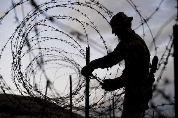 The silhouette of an NZDF member and a barbed wire fence