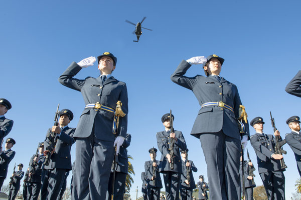 Air Force personnel on parade, two at the front standing to attention, a helicopter is overhead